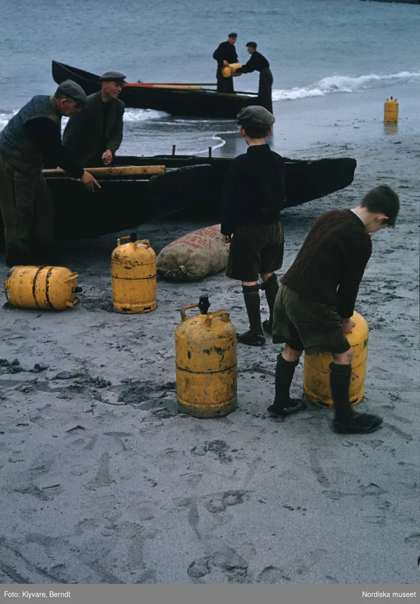 Strand på Irland. Män och pojkar lastar gasolflaskor från roddbåtar.