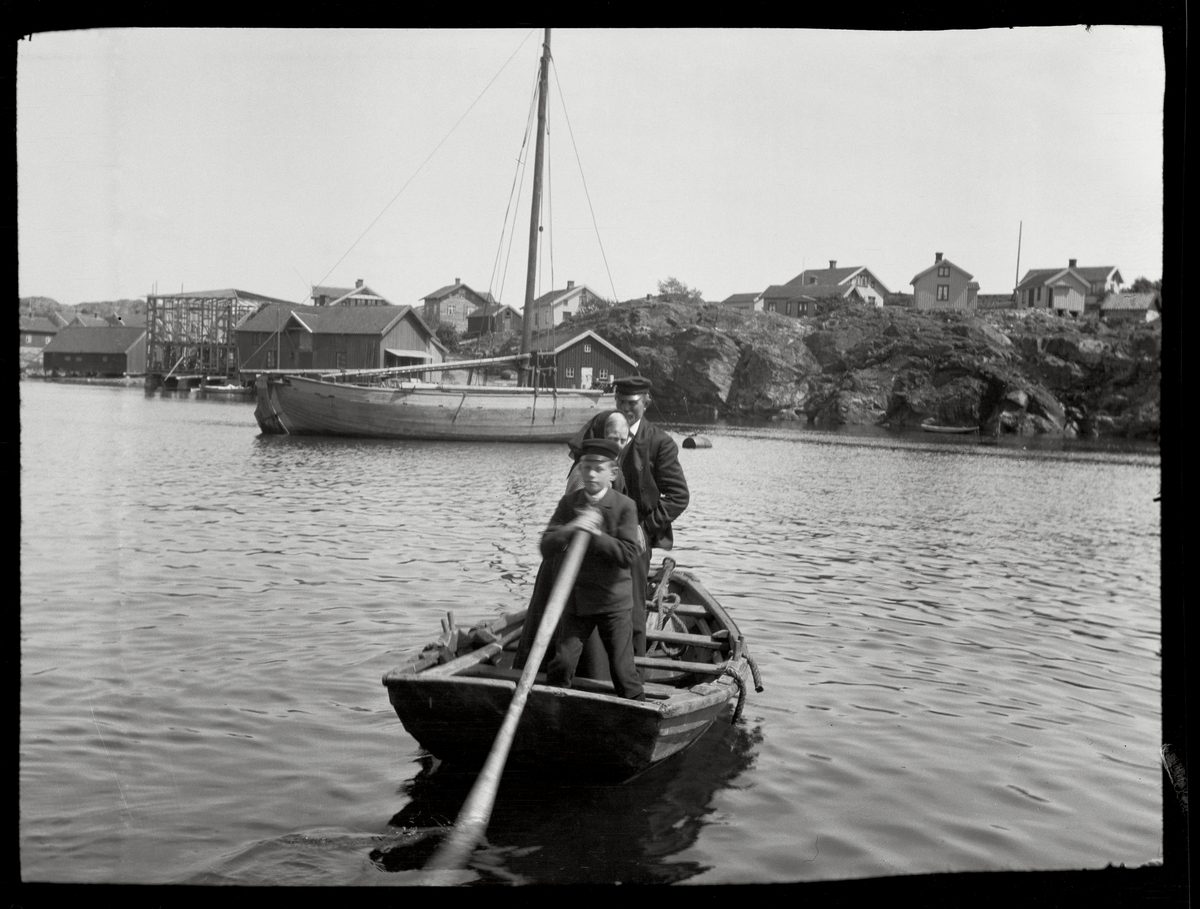 Pojke med åra och två personer stående i liten båt.