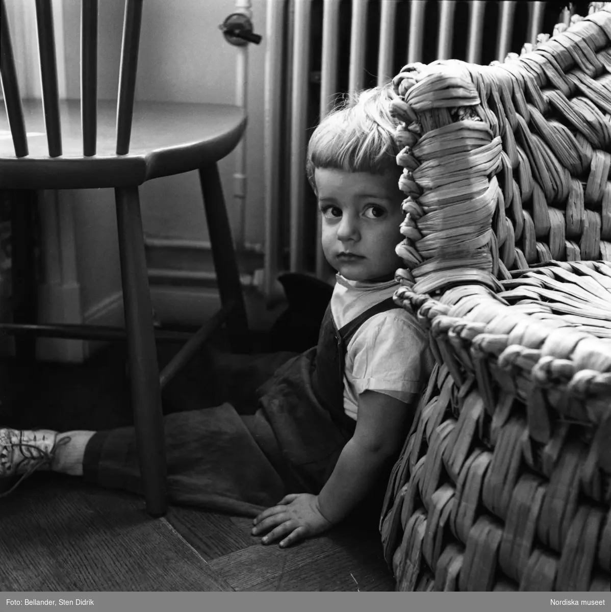 Fotografens son Tom sitter på golvet vid en korgstol.