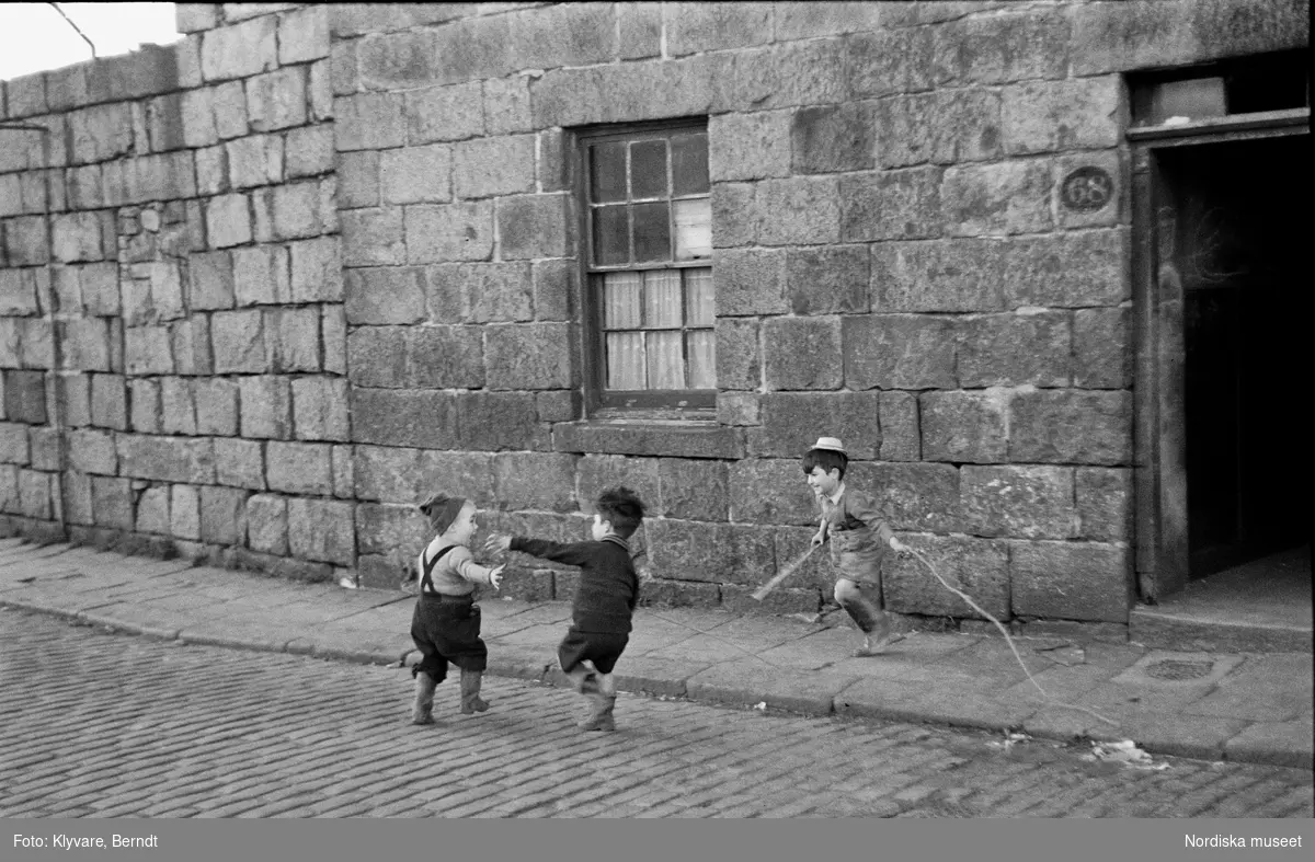 Tre små pojkar leker på stenbelagd gata, Shetlandsöarna.