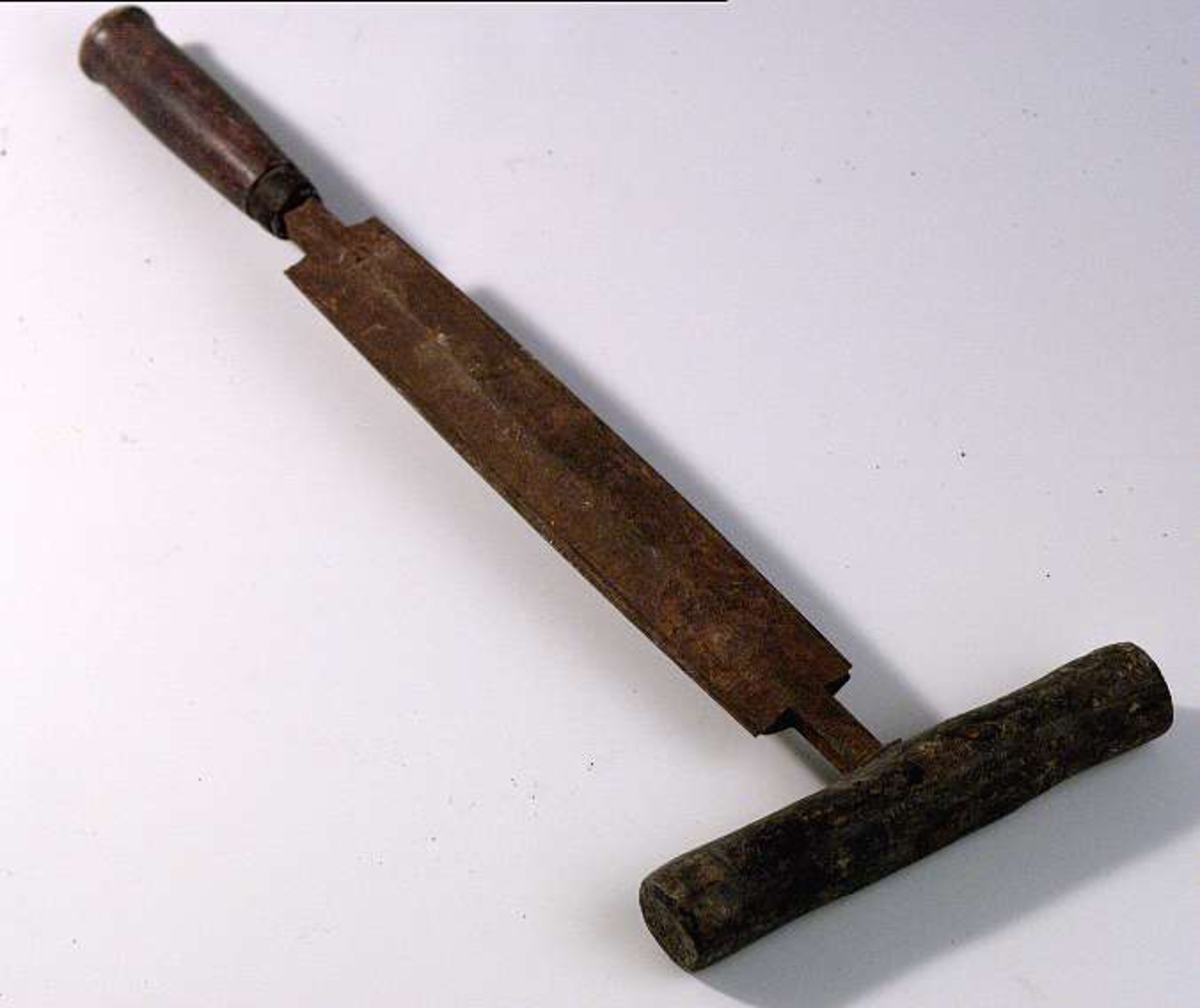 Falskniv av järn med två smala eggar fastskruvade, ett rakt och ett tvärställt handtag av trä.