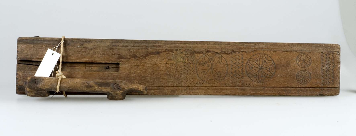 Mangelbräde av trä, dekorerat med sicksackmönster och fyra stjärnor. Inskrift: ANO 1753 AOS KMD. Handtag som påminner om en häst. Märkt B 881 samt etikett med handskriven text: Roslagen, Rimbo sn.