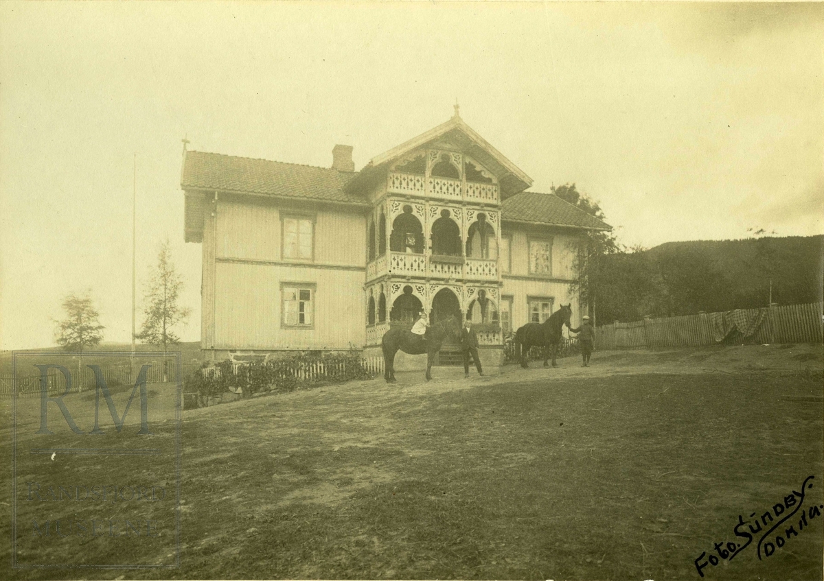 Våningshus sveitserstil, to hester og tre personer oppstilt foran inngangen.