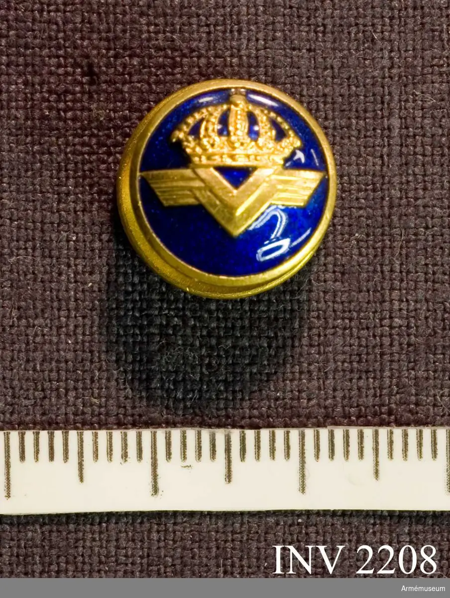 Av guld och blå emalj med verkets emblem i guld. Platt hals fäst vid en något större platta (större än knappen, d 15 mm)  märkt "128". Bärs i slagets knapphål.
Styresman O Cederlöf har i egenskap av f d flygare fått bära  denna knapp.