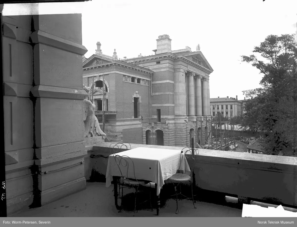 Bord med duk og tre stoler på veranda på Hotel Continental, Nationaltheateret og Universitetet ii bakgrunnen