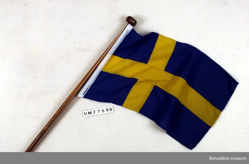 Akterflagg  - svenska flaggan -  i bomull på lackad mahognystång med knopp för fastsättning i aktern på snipan Lisen (UM27596). Med flagglina av nylon.
Båten visas i Båthallen, Bohusläns museum.

För uppgifter om båten och förvärvet, se UM27596.

Se uppgifter under Placering.