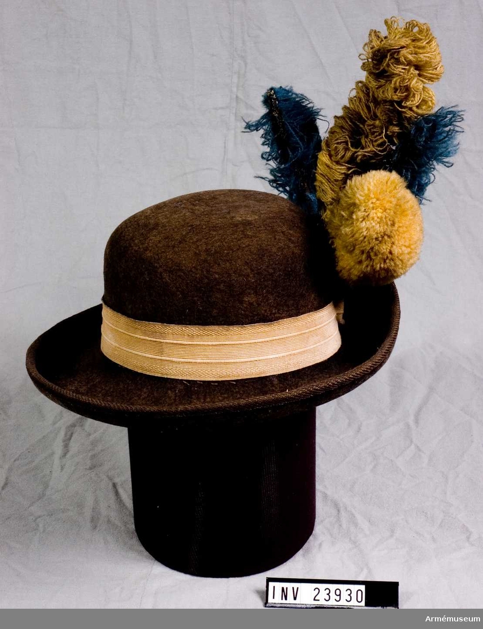 Hatt av svart filt med gult hattband och träns med knapp.