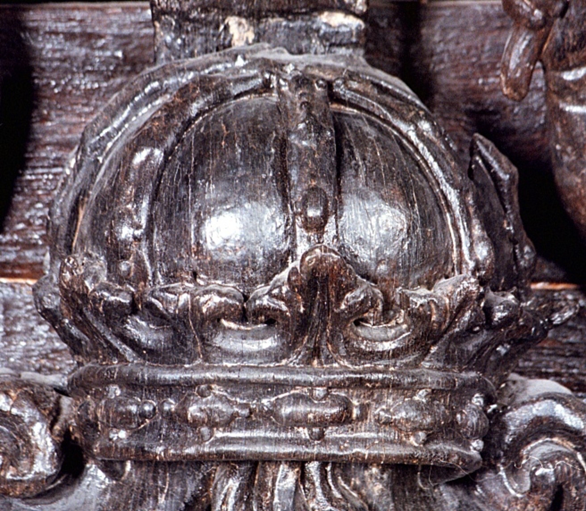 Skulpterad och profilerad sköld med kunglig krona och sädeskärve, vase. Skölden har förtjockade kanter och kraftiga rullverksformationer upptill och nedtill. Kärven är snidad med markerade strån och ax. Sköldens baksida är slät.

Text in English: Sculpted shield depicting the royal crown and a sheaf of corn, (called Vase in Swedish), carved in relief. The shield is carved with thickened edges and scrollwork formations at the bottom and top. The crown is shown in perspective and the stalks of the corn in the corn sheaf are clearly defined. The reverse side of the shield is smooth.