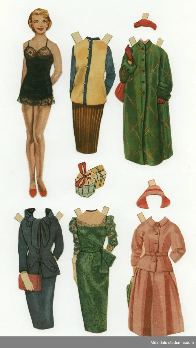 Pappersdocka med kläder och tillbehör, urklippta ur tidning på 1950-talet. Docka och kläder är märkta "Maj-Britt" på baksidan - dockans namn. Dockan föreställer en kvinna med blond frisyr, iklädd svart underklänning och röda skor. Garderoben består av tre set med kjol och tröja/jacka, golfkläder (ärmlös blus och kjol), två vadlånga aftonklänningar, tre balklänningar, två kappor, samt två hattar. Dockan har också paket som tillbehör. Docka och kläder förvaras i ett vitt C6-kuvert, märkt "Maj-Britt", men ursprungligen poststämplat i Åbo, Finland 1954, till familjen.