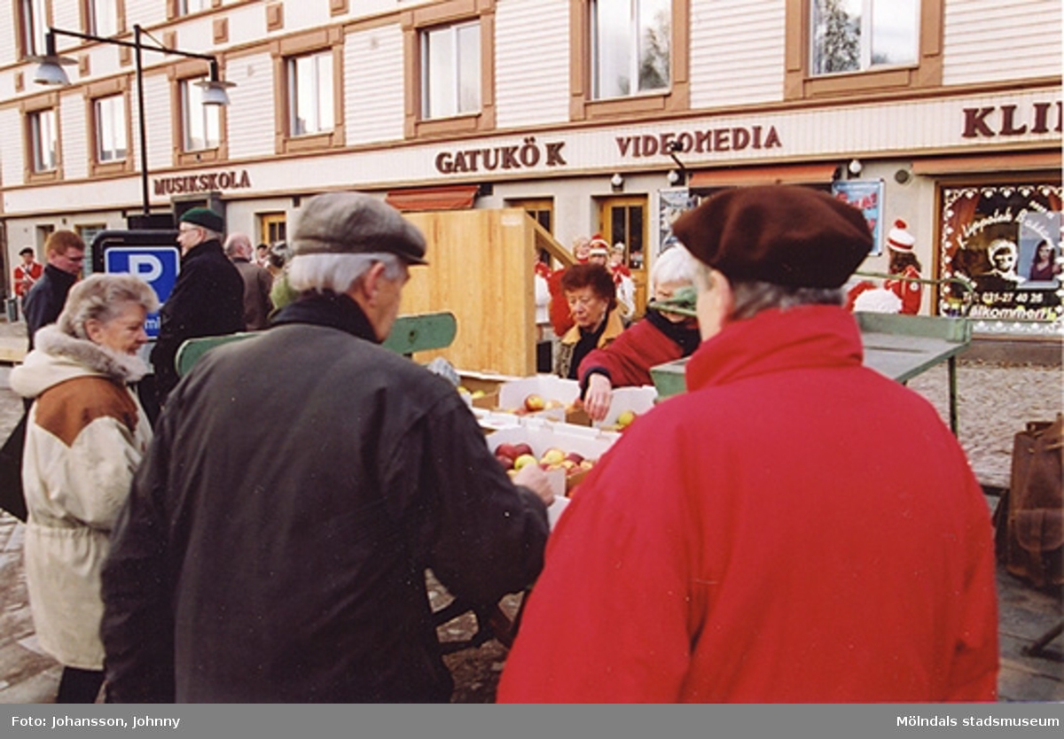 Gamla torget i Mölndal den 22:a november 2001. Folk plockar frukt från ett stånd.
Invigning efter omläggning och stenläggning av torget. I bakgrunden till vänster står politikern Patrik Karlsson och samtalar med en man.