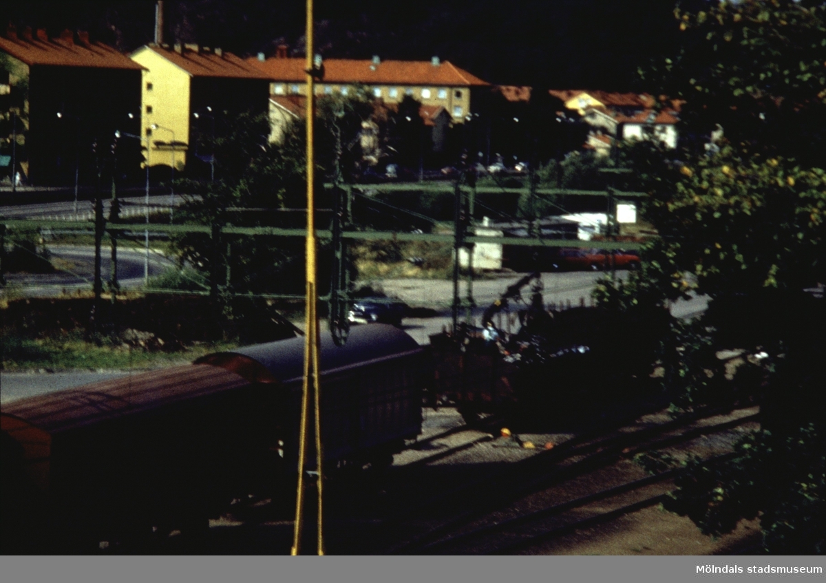I förgrunden ses en del av järnvägsområdet, i bakgrunden fastigheter vid Göteborgsvägen (Bosgården) i Mölndal, 1970-tal.