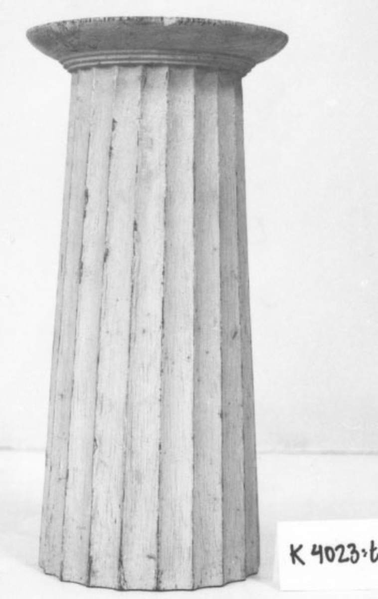 Pelare, eller kolonner, släta och räfflade (7 st halvkolonner, räfflade). 20 st. modeller av trä, avsedda som fasadprydnader. Pelarna är räfflade med halvcirkelformig basyta. De är vitmålade. Kapitälen är av närmast dorisk stil. Pelarna utgör modeller till gavelkonstruktion för nya inventariekammaren på varvet 1785-87. De sammanhängs troligen med en serie av gavelmodeller och pelare, som finns i kistan i sal 1 och vid norra delen av väggen i samma sal. (K 2244)

3/4 Kolonn, kannelerad, med kapitäl, målad i gråvitt.

Bas D = 90mm  Kapitäl D = 108mm
