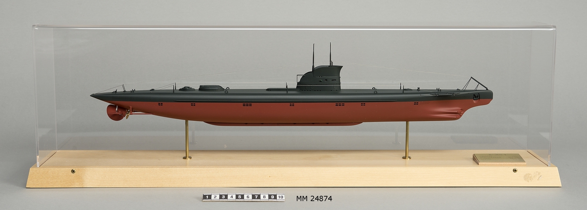 Ubåtsmodell Hajen II i monter. Modell av alträ med detaljer av mässing, målad med cellulosafärg. Rött och svart skrov. Monter av plexiglas på träplatta. Mässingsbricka i montern med uppgifter om modellen.