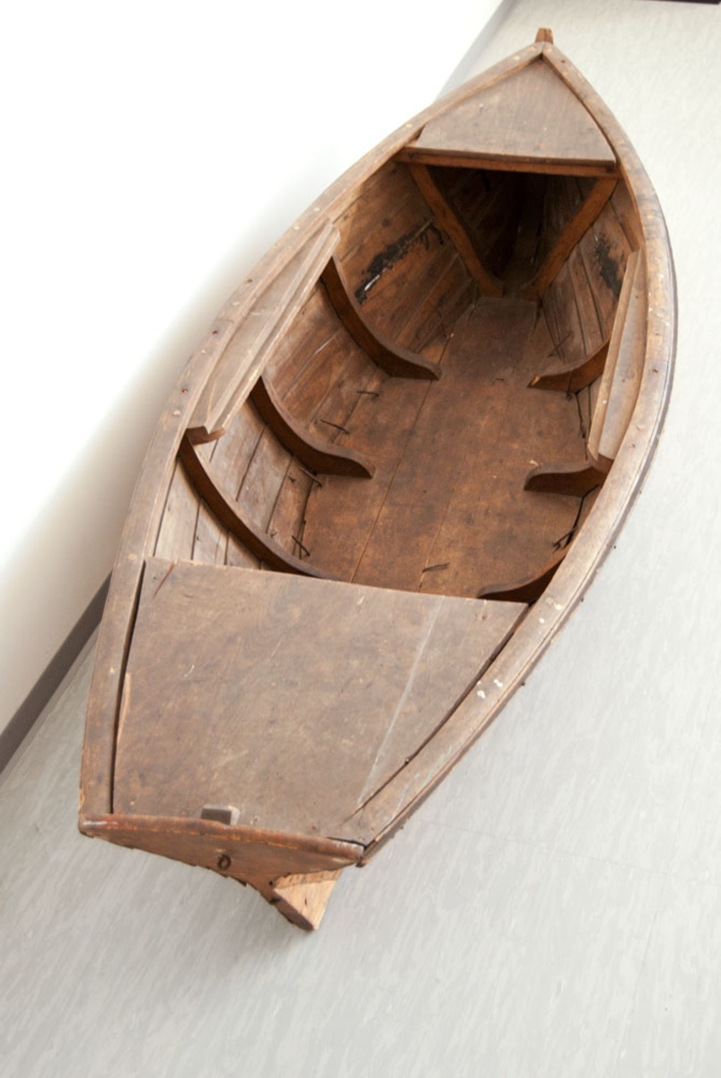 Liten båt brukt i scenografi ved E. H. Torjusens atelier.
Båten er i tre, gliper mellom bordene. Spikre slått gjennom bunnen.
