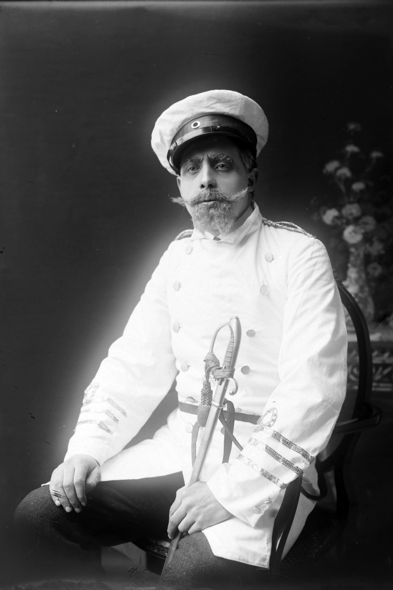 Studioportrett av en mann i hvit uniform som holder på en sabel.