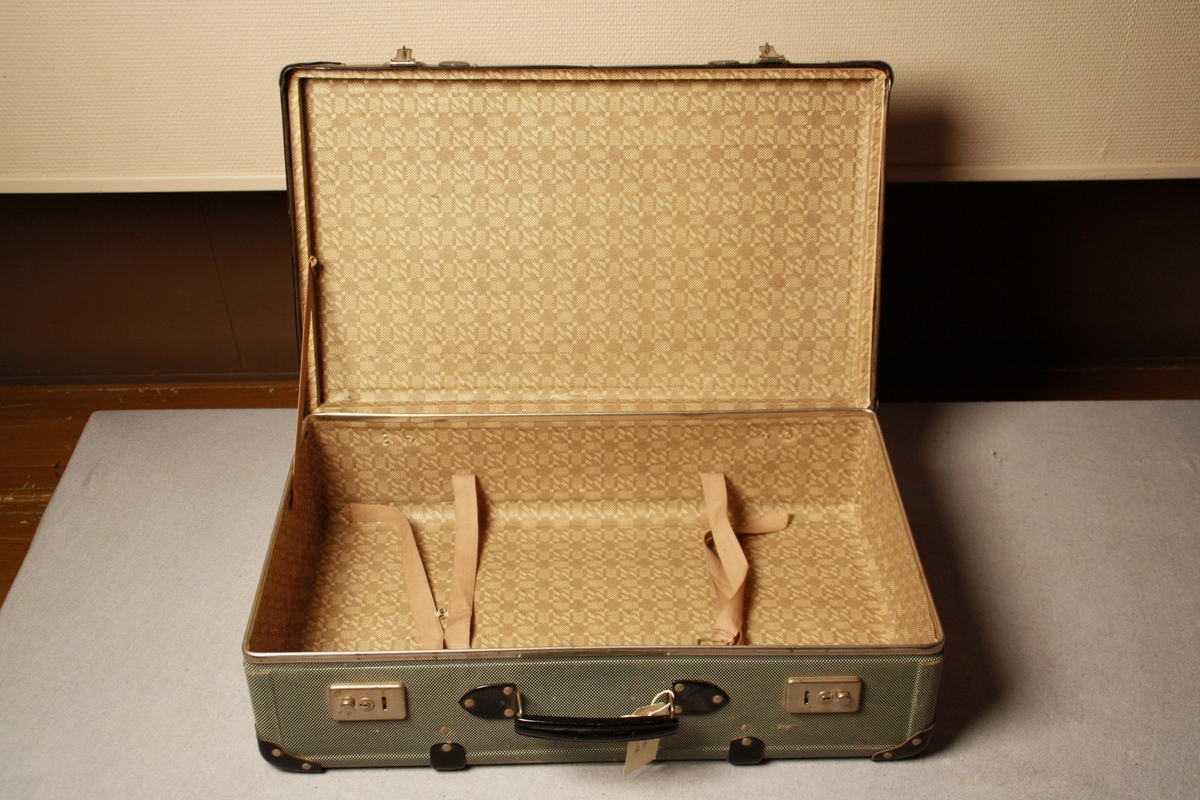 Koffert i papp, grå med kvite prikkar utvendig, beigemønstret inni. Svarte metallforsterkingar i hjørner og kantar, svart handtak. Metallås med Viking rissa inn