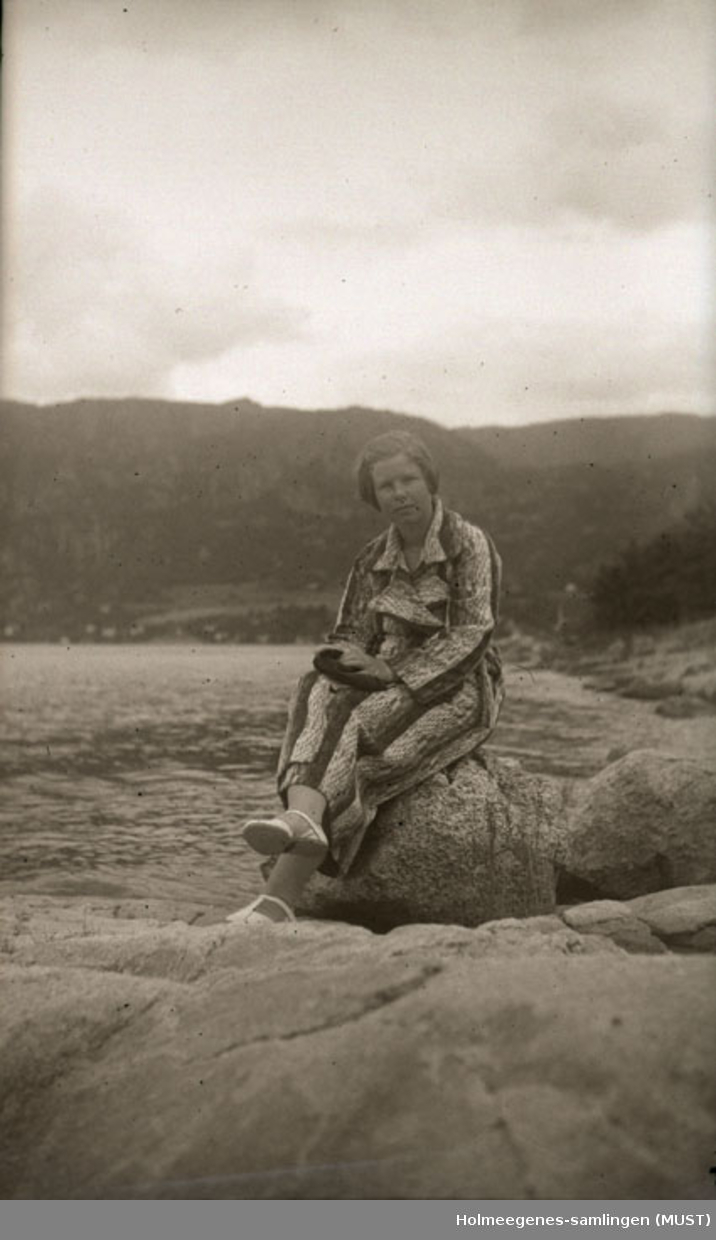 En ung kvinne kledd i en slags badekåpe sitter på et svaberg.