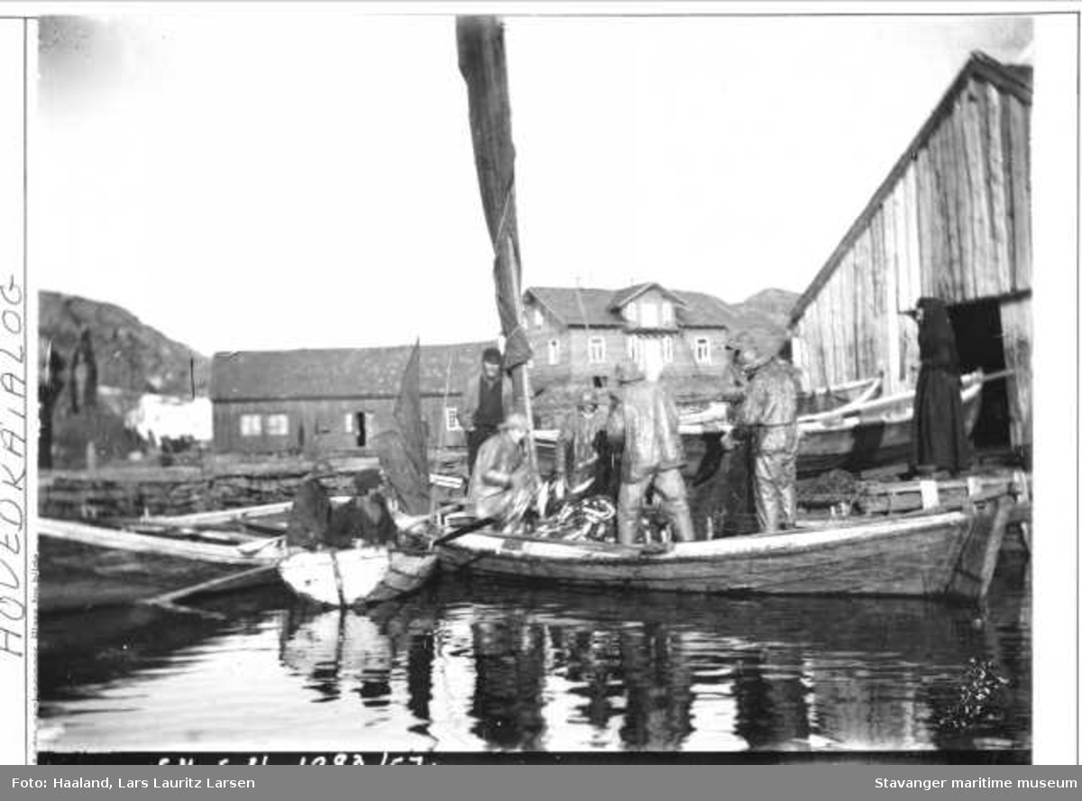 Fiskere som har kommet inn til Ydstebøhavn med sild. Lauritz Haalands villa ligger midt i bildet til høyre, det er under bygning. Bildet er tatt ca 1885. 