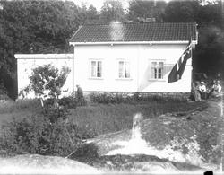 Lite, hvitt hus med flagg. Kvinner og mann ved huset