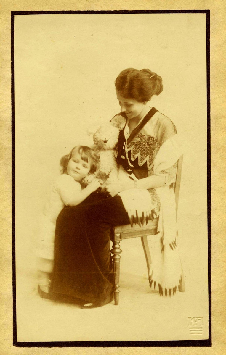 Kvinne i stol med bamse på fanget, liten gutt ved siden