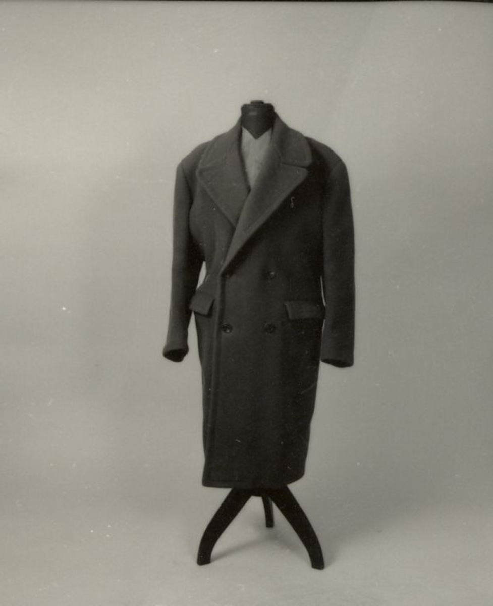 Frakk av tykk ull, med paspoilerte lommer og spensel bak. 4 knapper foran.