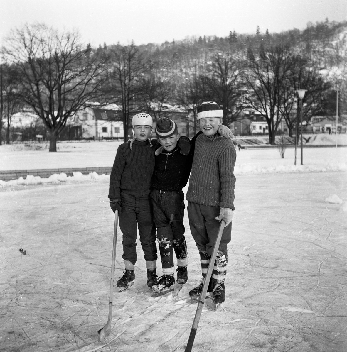 Från vänster, med skridskor och ishockeyklubba, står Per "Pelle" Andersson, Gunnar Westin och Tom Andersson på isen i Mjölkafållan i Huskvarna.