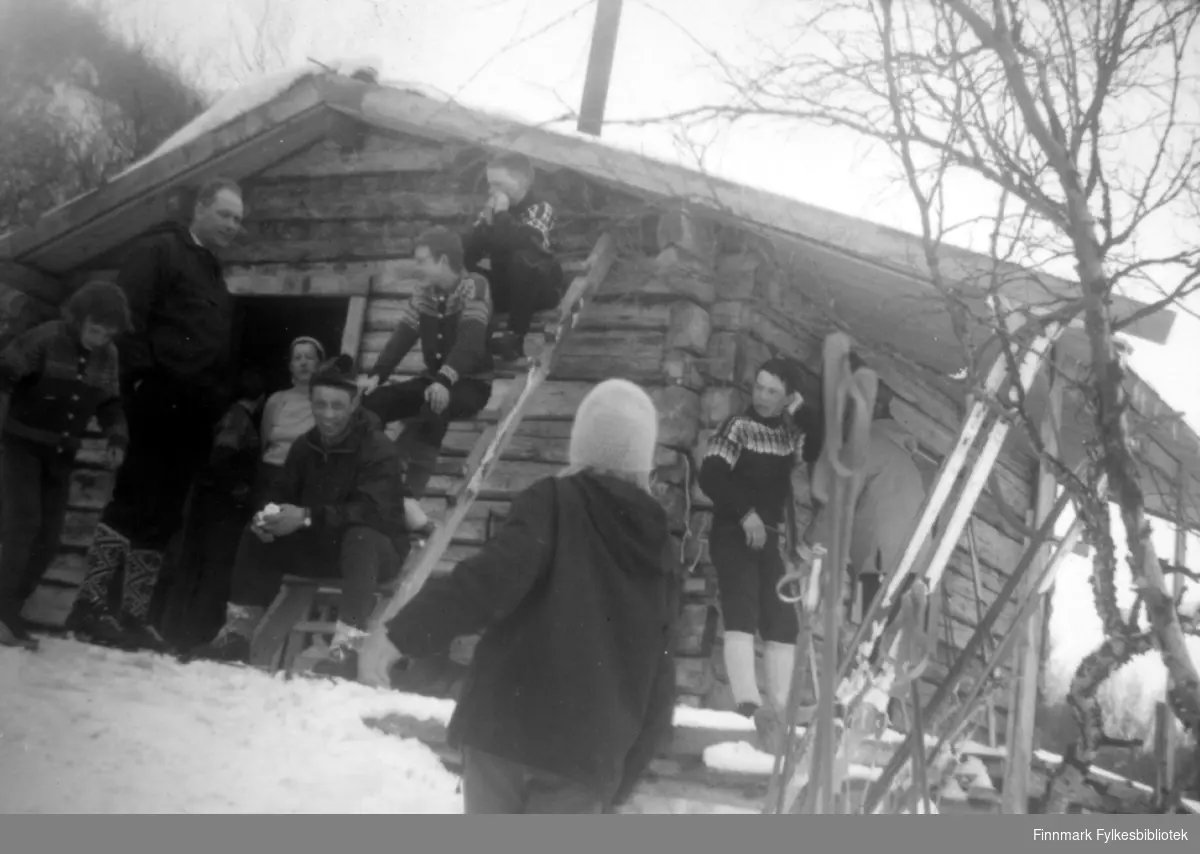 En liten gruppe mennesker utenfor en hytte. Personene er ukjent, men hytta kan være i Rochi i Porsanger.