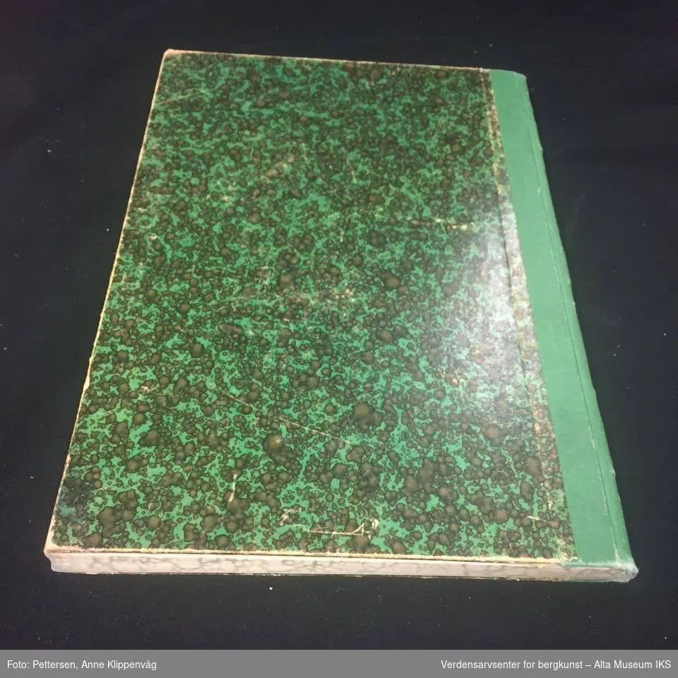 Rektangulær notatbok, innbundet med harde permer. Grønn og sortmønstret på forsiden og baksiden.