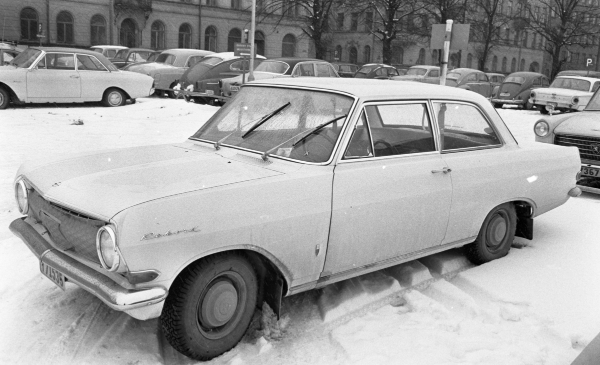 Bilar, Bilnummer, Bilhall 30 mars 1966

. 
Bilen är en Opel Rekord. Bilparkeringen har adressen Nygatan 7. I bakgrunden syns korsningen Fabriksgatan och Nygatan.