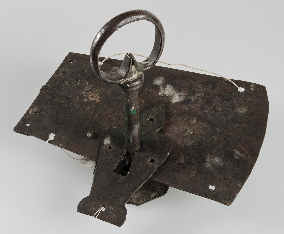 Fällbomslås med tillhörande nyckel och profilerat slutbleck, smitt av järn. Nyckeln är s.k. vridlåsnyckel med ögla (grepp).



