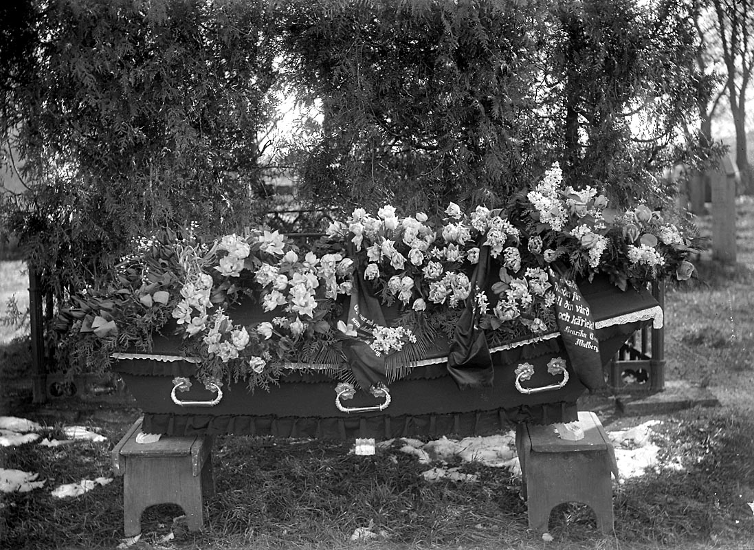 Begravning, likkista och begravningskransar.