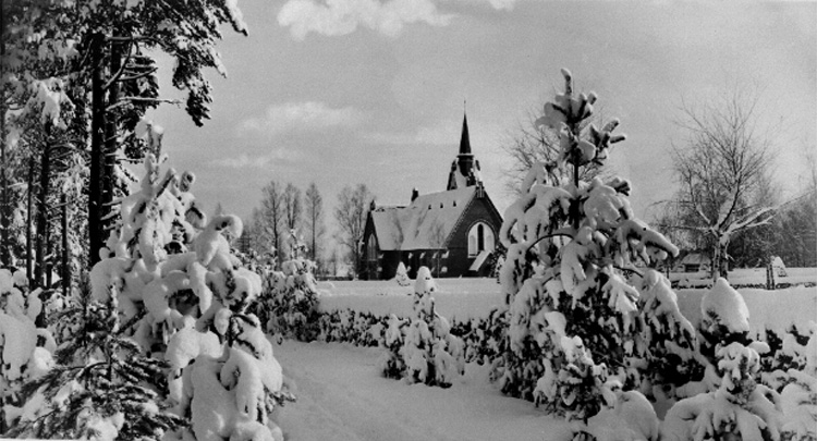 Kyrkobyggnad.
Vintermotiv, snötyngda granar.