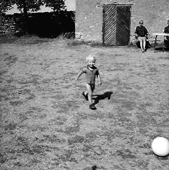 Familjegrupp framför huset.
En liten pojke leker med bollen.