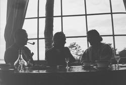 To kvinner og en mann sitter ved et bord med glass, kopper o