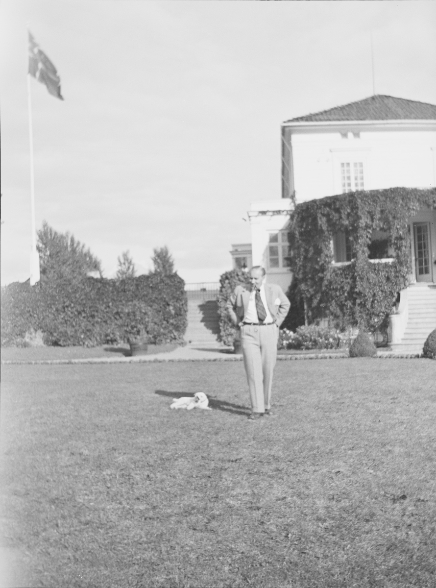 Iacob er fotografert på plenen i den victorianske hagen. En hund ligger rett ved ham. Flagget er heist.