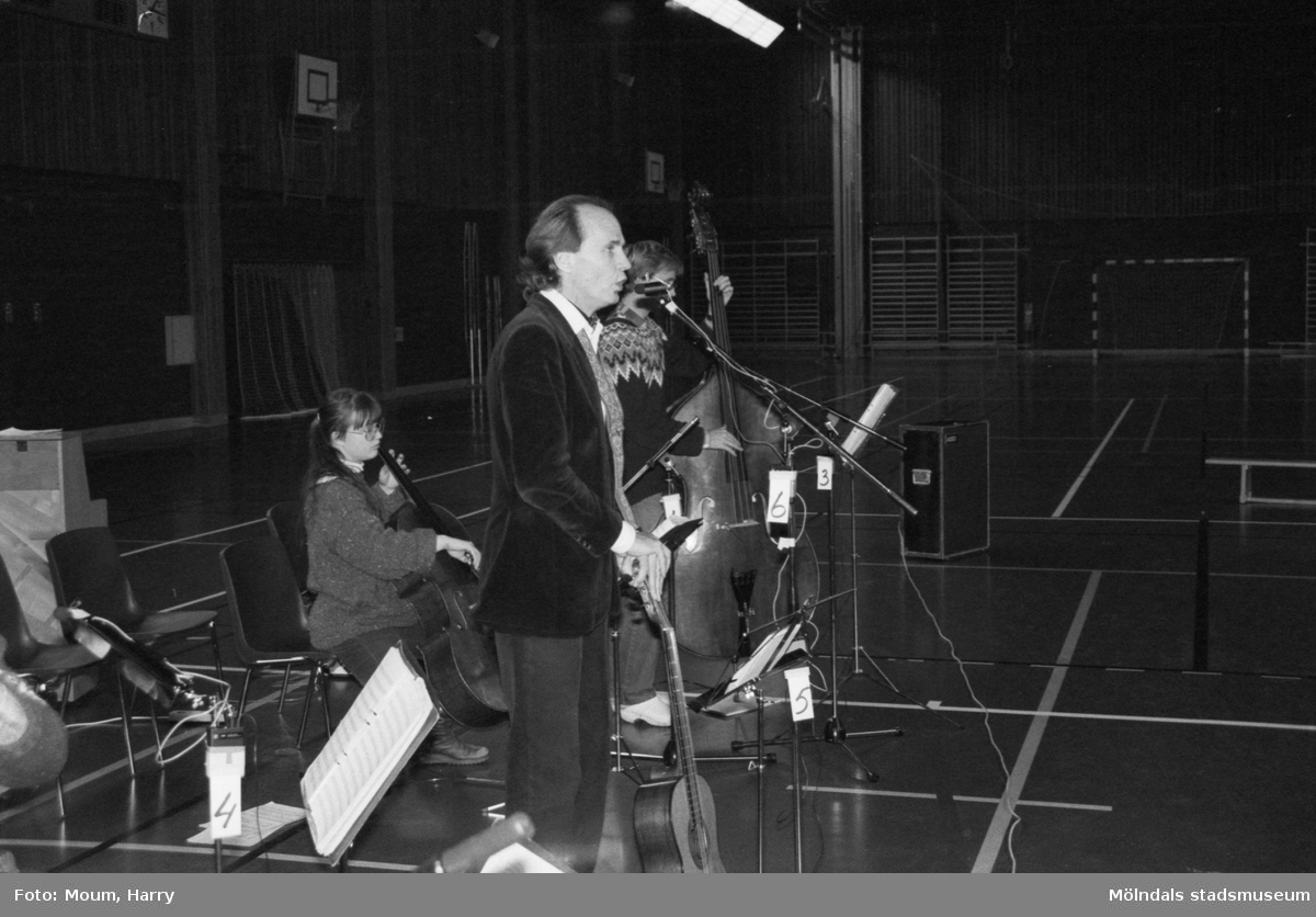 Trubaduren och viskompositören Alf Hambe håller tillsammans med gruppen Vindharpan konsert i Ekenskolans gymnastiksal i Kållered, år 1983.

För mer information om bilden se under tilläggsinformation.