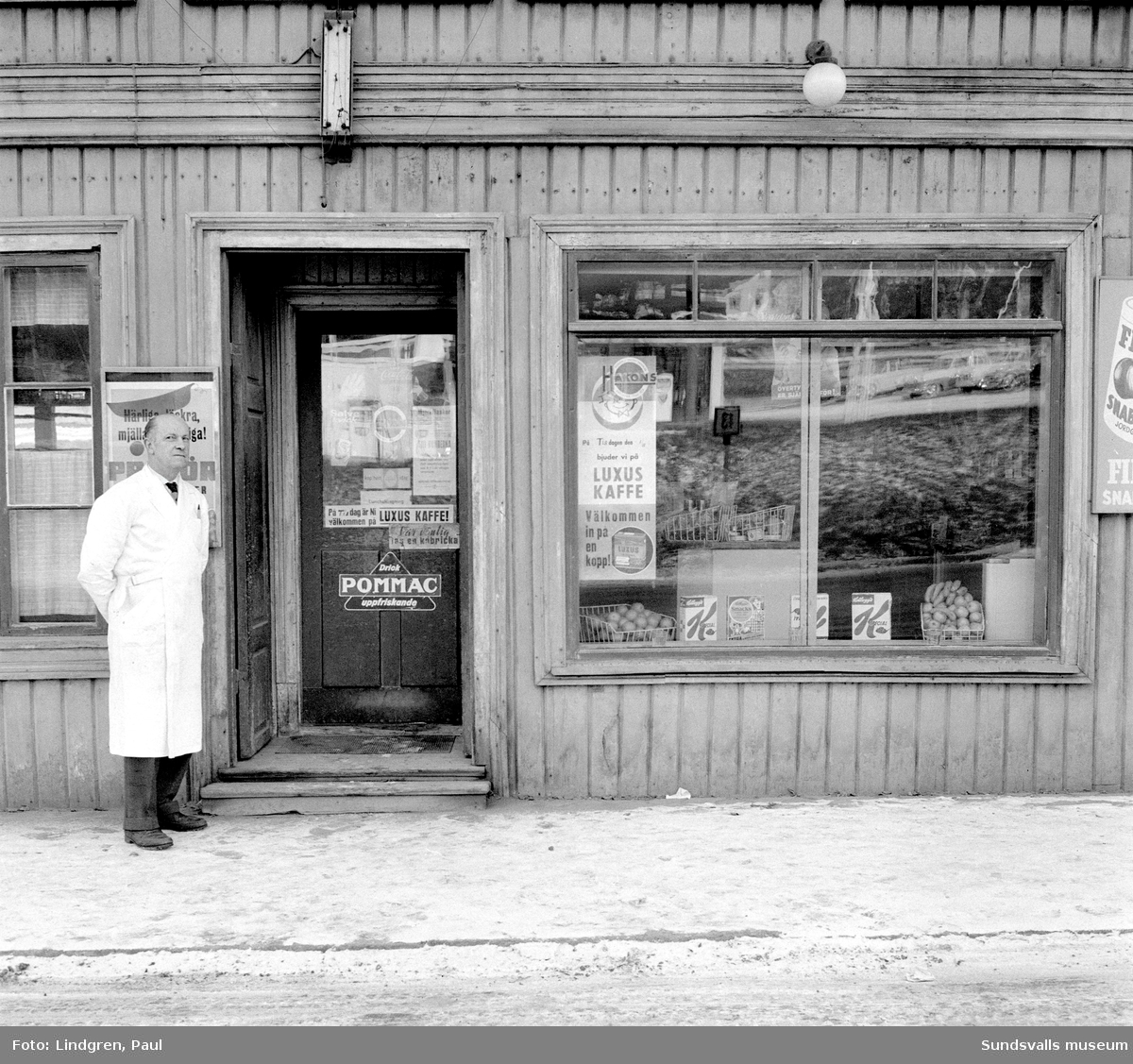 Livsmedelsbutik på Norrmalmsgatan 39. Här står butiksägaren Nils Olsson utanför butiken som först hans far A G Olsson och därefter han själv drev från 1920 fram till 1962. Bild 2 visar Nils Olsson vid kassaapparaten inne i butiken.