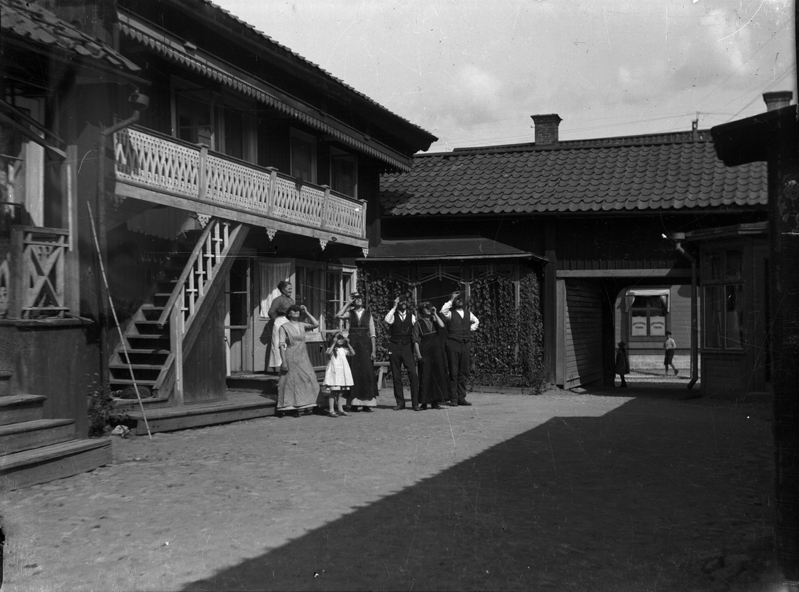 Bostadshus, hemmet på Kungsgatan 33, Lindesberg.Grupp sju personer framför huset, troligen solförmörkelsen den 21 augusti 1914.Från vänster Eva Sofia Pettersson (givarens farmor), Ester Pettersson, Kerstin Pettersson (givarens fastrar), övriga ej namngivna.