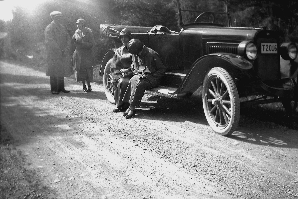 En bil, fyra personer vid bilen. 
Bilen är en Overland Four som ägdes av skräddaremästare A. J. Pettersson, Lindesberg. Den hade registreringsnummer T2016 och registrerades den 25:e april 1923 med honom som ägare. År 1930 finns bilen kvar i bilregistret, men ägs numera av Viktor Teodor Johansson, Bofors.