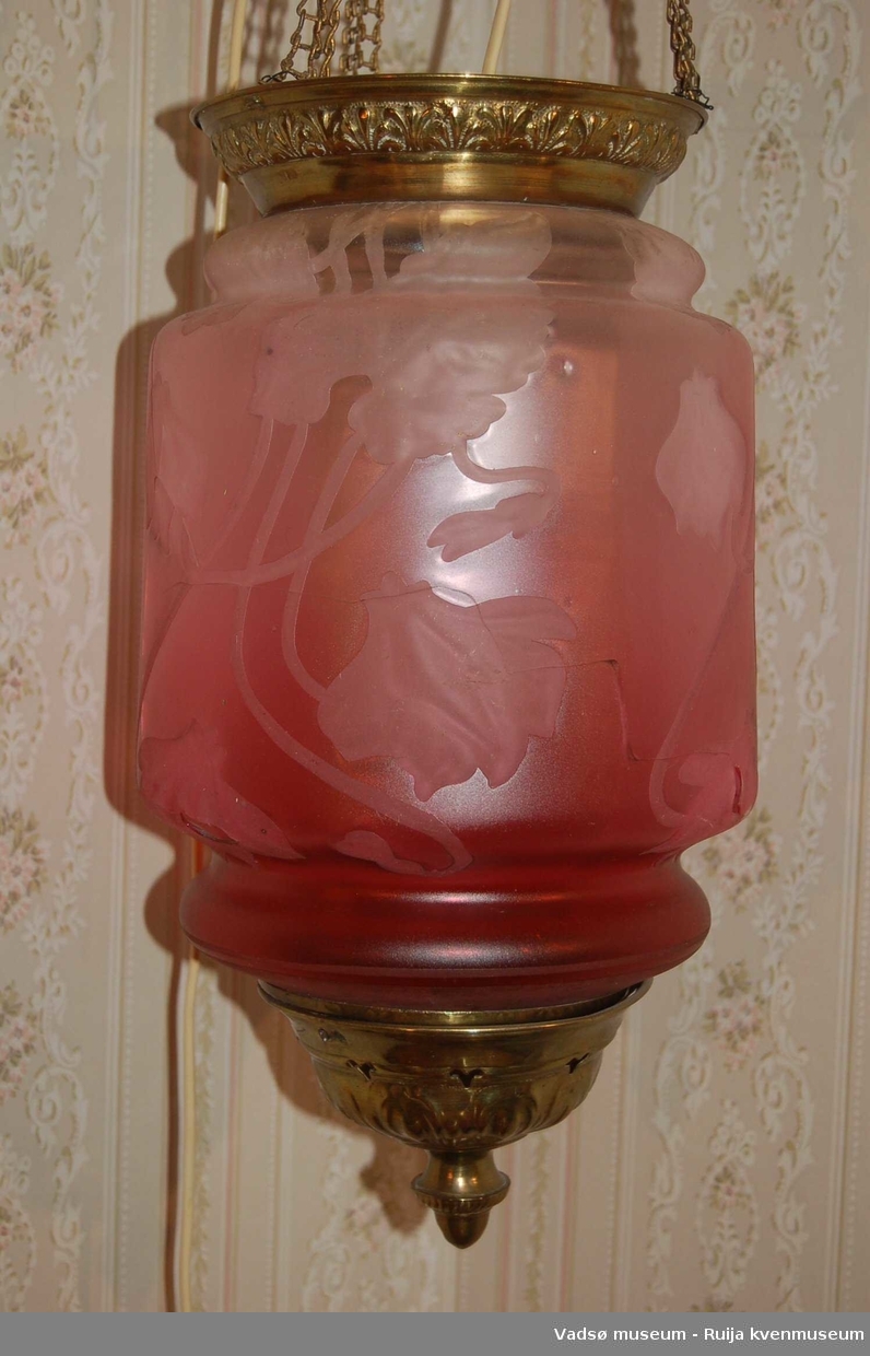 Sylinderformet måneskinnslampe i rosa glass og messing. Glasset har blomsterdekor i relieff. Lampehuset henger i fire messinglenker som går til et sirkulørt takfeste. Lampas øvre kant, bunnstykke og takfestet er i messing.