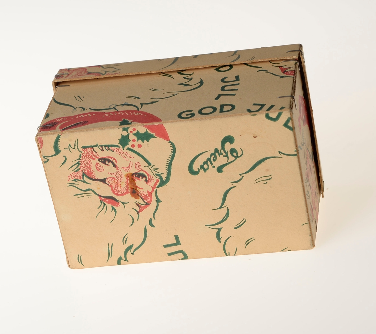 En liten pappeske med lokk som har vært emballasje for en marsipangris. 
På esken er det logoen til Freia, julenissemotiv og så står det God Jul. Inni esken ligger det silkepapir (antageligvis originalt).