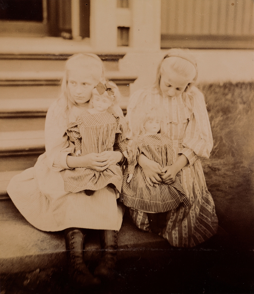 Eva og Minnie (Emilie) Christensen sitter på trapp og leker med dukkene sine.