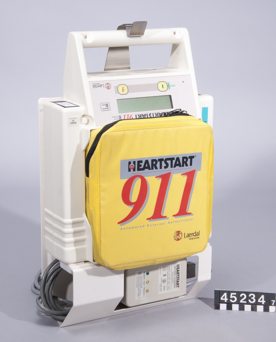 Defibrillator för undersökning av hjärtrytm och vid behov defibrillation med påföljande stimulering av hjärtat.  Apparaten används enligt följande, förenklat: Patienten har förlorat medvetande, andning och puls. Självhäftande elektroder fästs på patientens bröstkorg, apparaten startas. Om utrustningen känner av att elektroderna är rätt fästa ger den efter ca 15 sekunder anvisning om att användaren ska trycka på knappen för "analys". Användaren varnas också med ett röstmeddelande för att röra patienten under analysen. Om utrustningen detekterar en behandlingsbar arytmi laddas den upp och ger röstmeddelande om att knappen för en chock ska tryckas ner. Sedan ber utrustningen om analys igen. Cykeln upprepas om ingen puls registeras.  Apparatväskan är utrustad med följande tillbehör: plasthandskar, rakhyvel (Bic engångshyvel), torkdukar, våtservetter och en förpackning elektroder.  Med apparaten följer också en laddstation att montera på vägg, heartstart 911 charging rack, cat nr. 901940. Batteri cat nr. 901100 "bäst före feb 2004". Cartridge för halvautomatisk drift, "Medical control module plus" cat nr. 920100, ser nr. 36026.