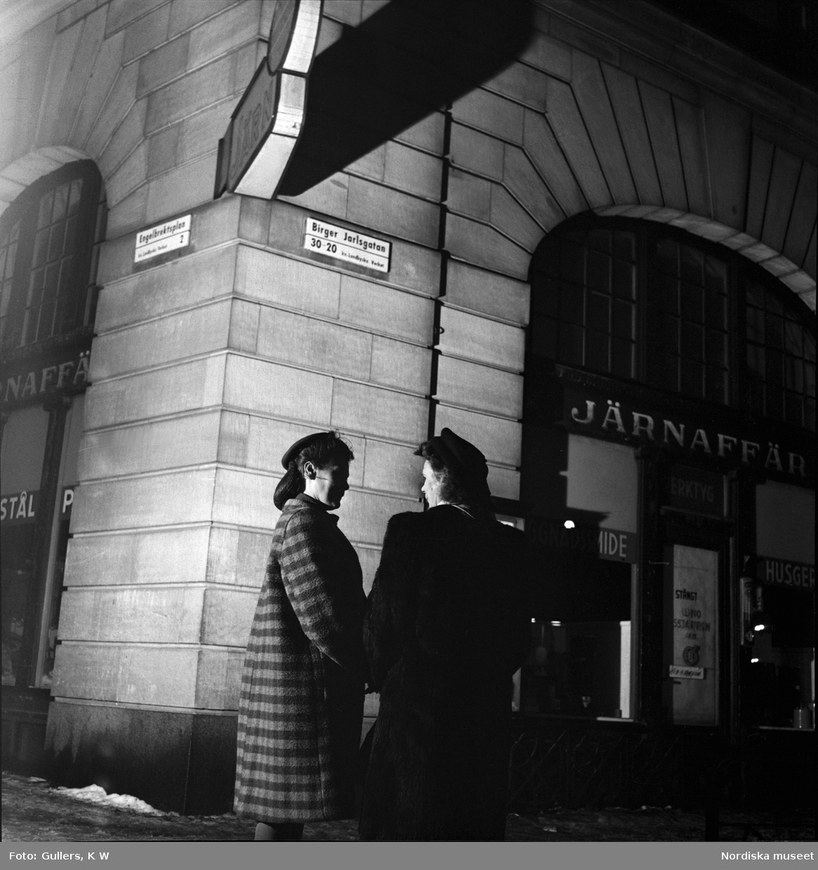 "Nattlivet börjar vid midnatt på Birger Jarlsgatan." Två kvinnor i samspråk på en trottoar i kvällsbelysning.