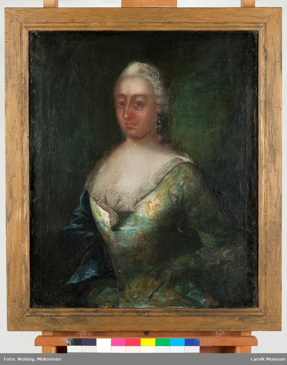 Portrett dame i grønn kjole m/gult mønster, hvit besetning i halsen, mørkegrønn kappe