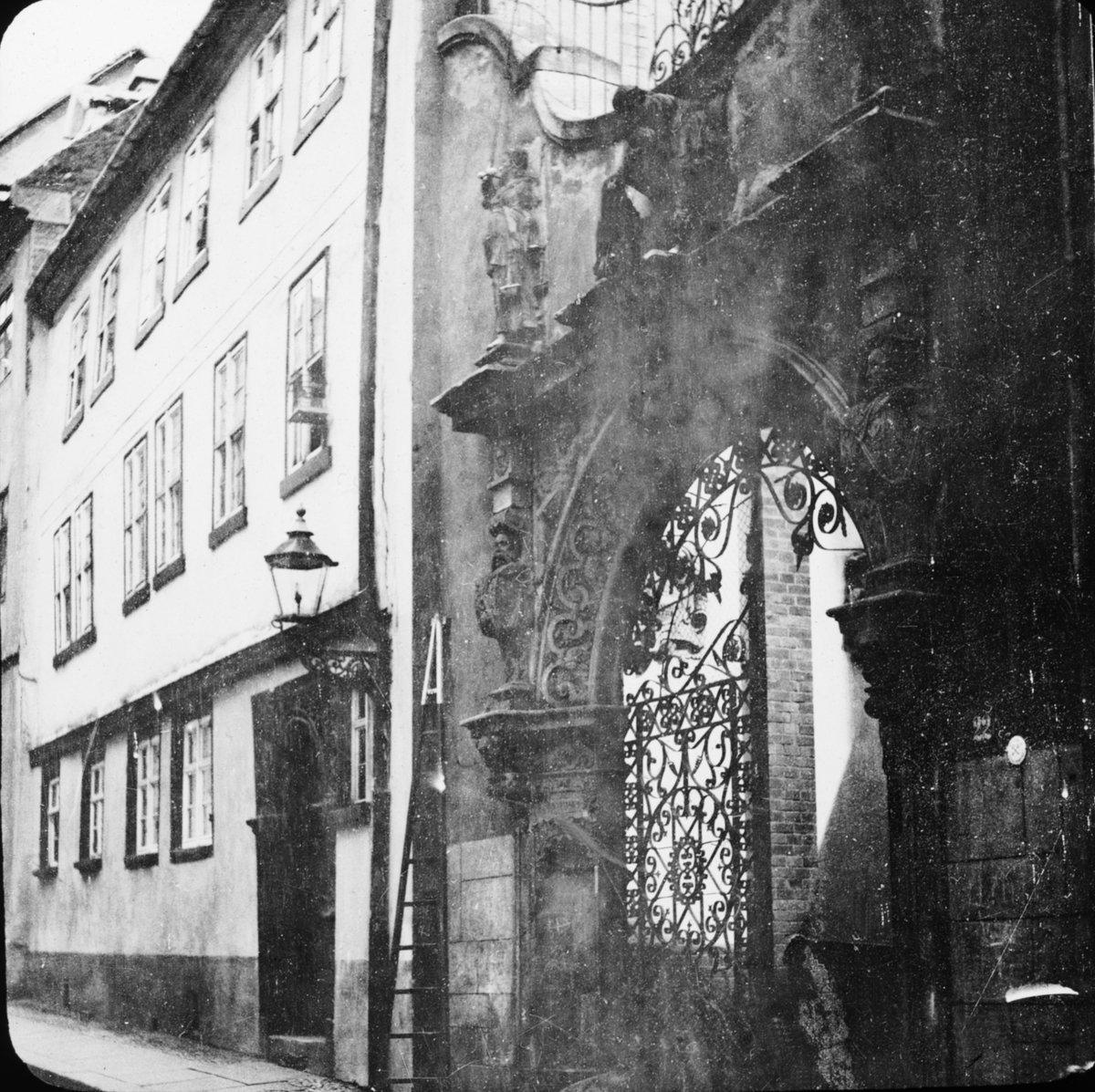 Skioptikonbild med motiv grind av smide längs gata i Bamberg.
Bilden har förvarats i kartong märkt: Resan 1907. Bamberg. 20