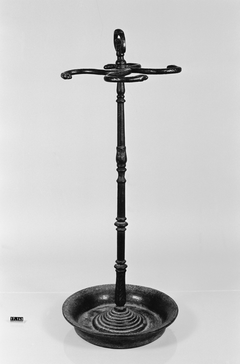 Paraplyställ av gjutjärn, med rund skål, ståndare med ornerat handtag, med fyra cirkelbågformade hållare med ormhuvuden.