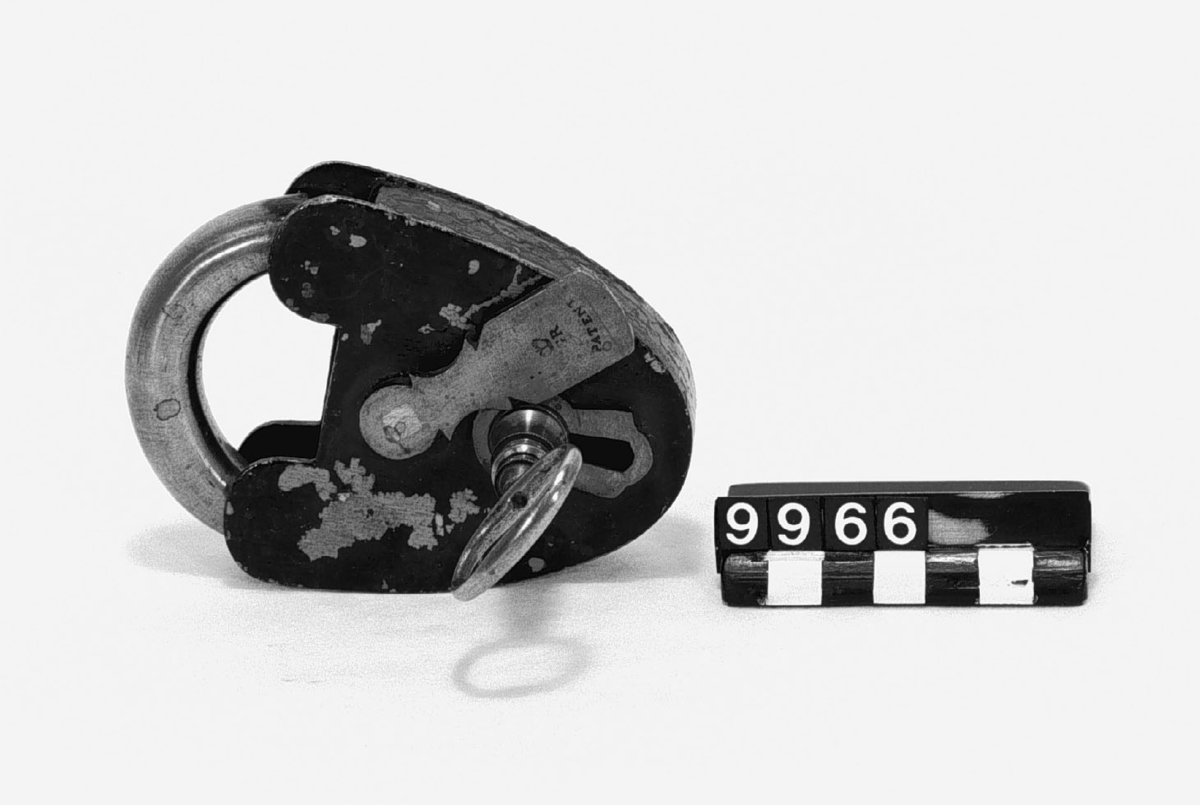 Platt hänglås av järn och mässing, lackerat. "820", " G R under krona Patent". Med en nyckel.