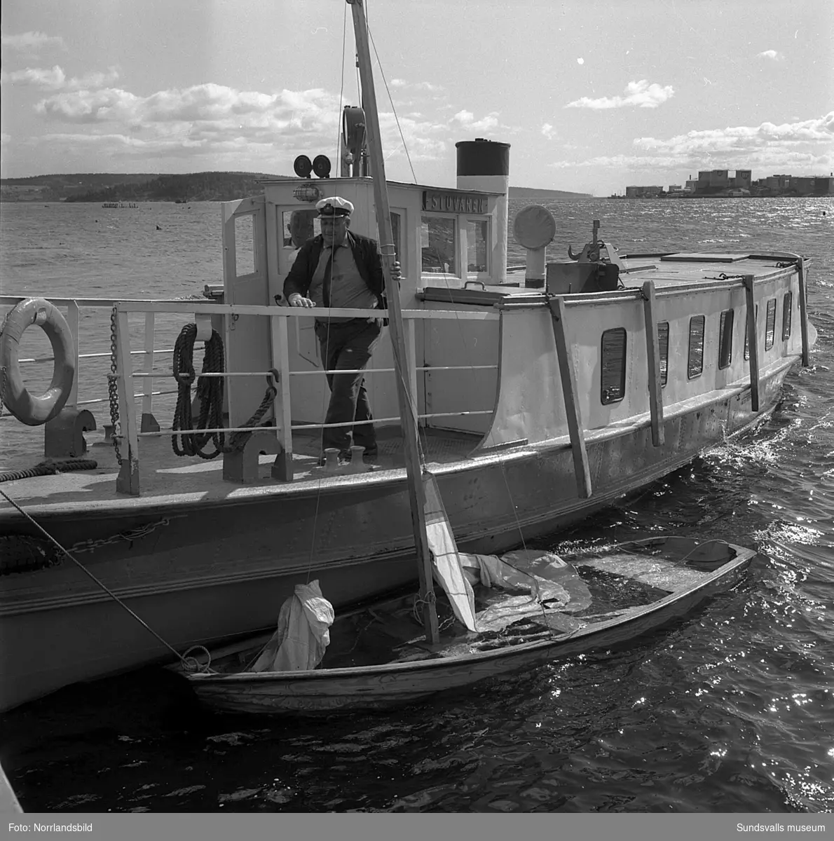 En liten kapsejsad segelbåt bogseras in i hamnen av båten Stuvaren.