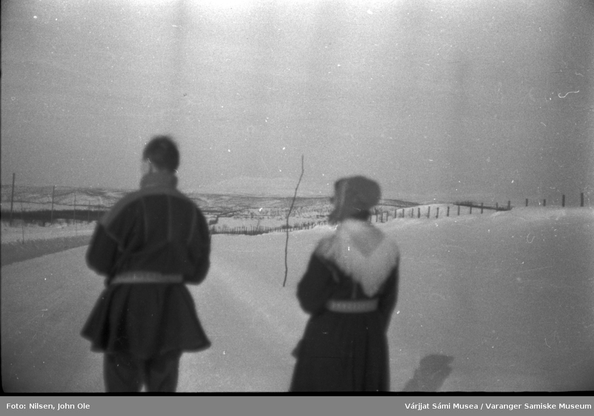 Par i kofte fotografert bakfra på en vei der de står og skuer bortover. Sannsynligvis John Ole og Signe Nilsen. Ukjent sted, 1966.